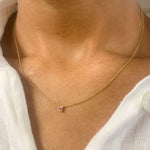 Woman in white top wearing a genuine July birthstone Ruby necklace in solid 14k yellow gold chain. In a prong setting, and natural red color. Best worn in a minimalist look, can be worn as an everyday necklace