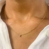 Woman in white top wearing a genuine July birthstone Ruby necklace in solid 14k yellow gold chain. In a prong setting, and natural red color. Best worn in a minimalist look, can be worn as an everyday necklace