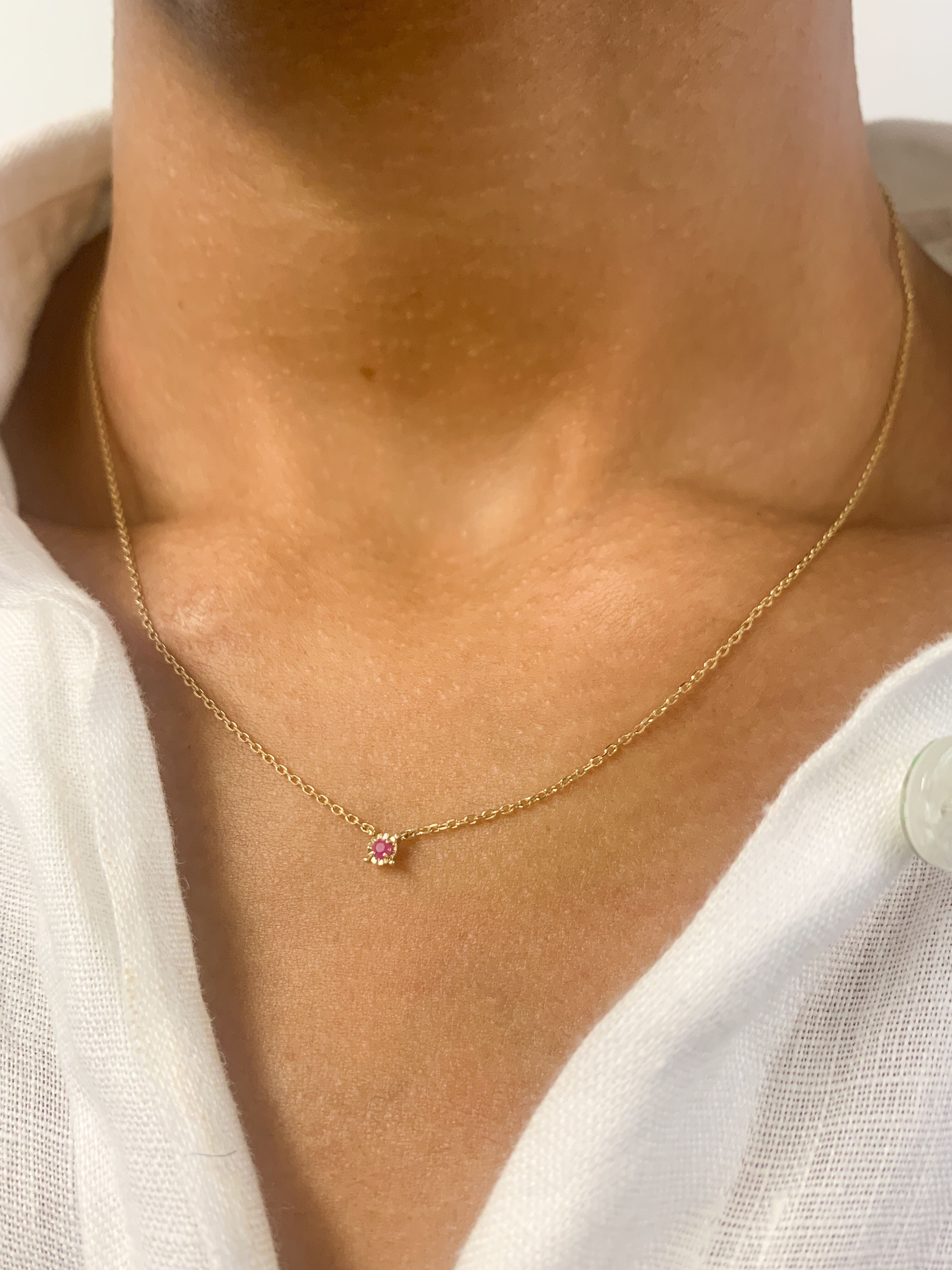 Woman in white top wearing a genuine July birthstone Ruby necklace in solid 14k yellow gold chain. In a prong setting, and natural red color. Best worn in a minimalist look, can be worn as an everyday necklace