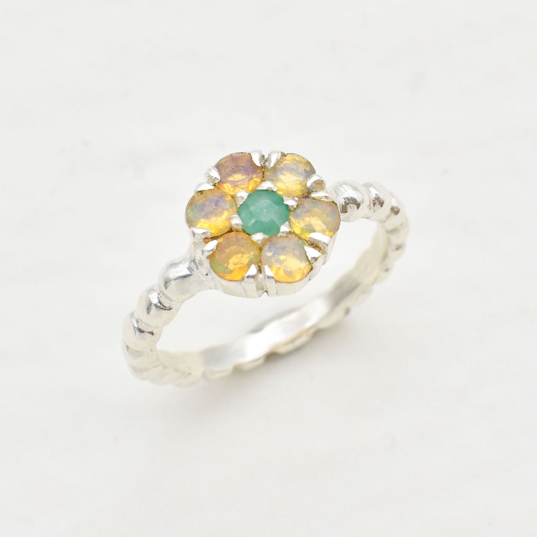 Natural Opal and Emerald Flower Ring in sterling silver with round-cut gemstones arranged in a floral setting. Jewelry style is elegant and unique with a handcrafted feel. Opal is known for inspiration and creativity while Emerald is linked to growth and harmony. A thoughtful October birthstone gift for birthdays, anniversaries, or meaningful occasions. Perfect to wear at weddings, family gatherings, formal dinners, or as a daily statement piece.
