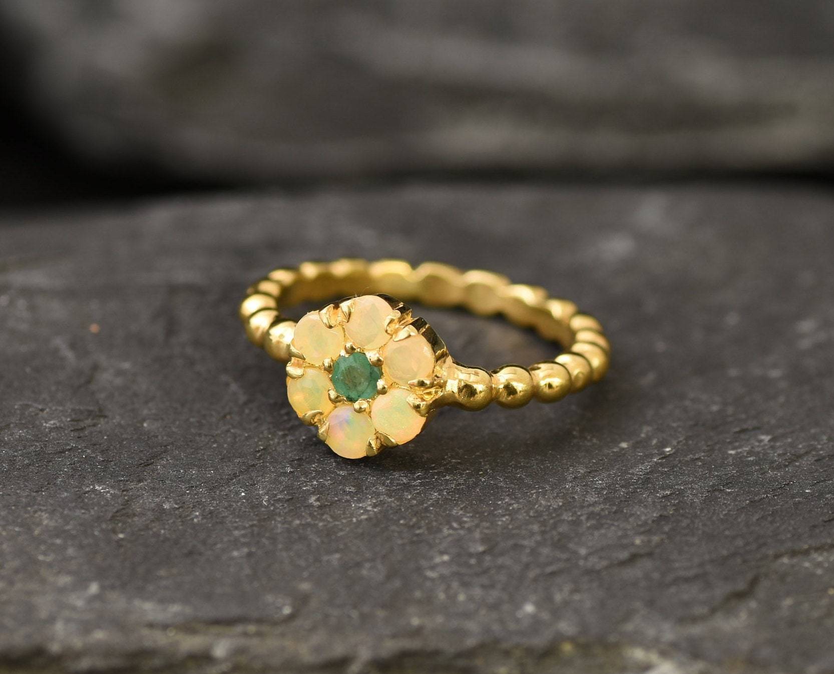 Natural Opal and Emerald Flower Ring in gold with round-cut gemstones arranged in a floral setting. Jewelry style is elegant and unique with a handcrafted feel. Opal is known for inspiration and creativity while Emerald is linked to growth and harmony. A thoughtful October birthstone gift for birthdays, anniversaries, or meaningful occasions. Perfect to wear at weddings, family gatherings, formal dinners, or as a daily statement piece.