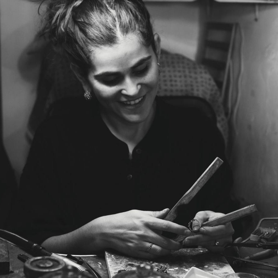 Black and white photo of a woman working with jewelry tools in a workshop.