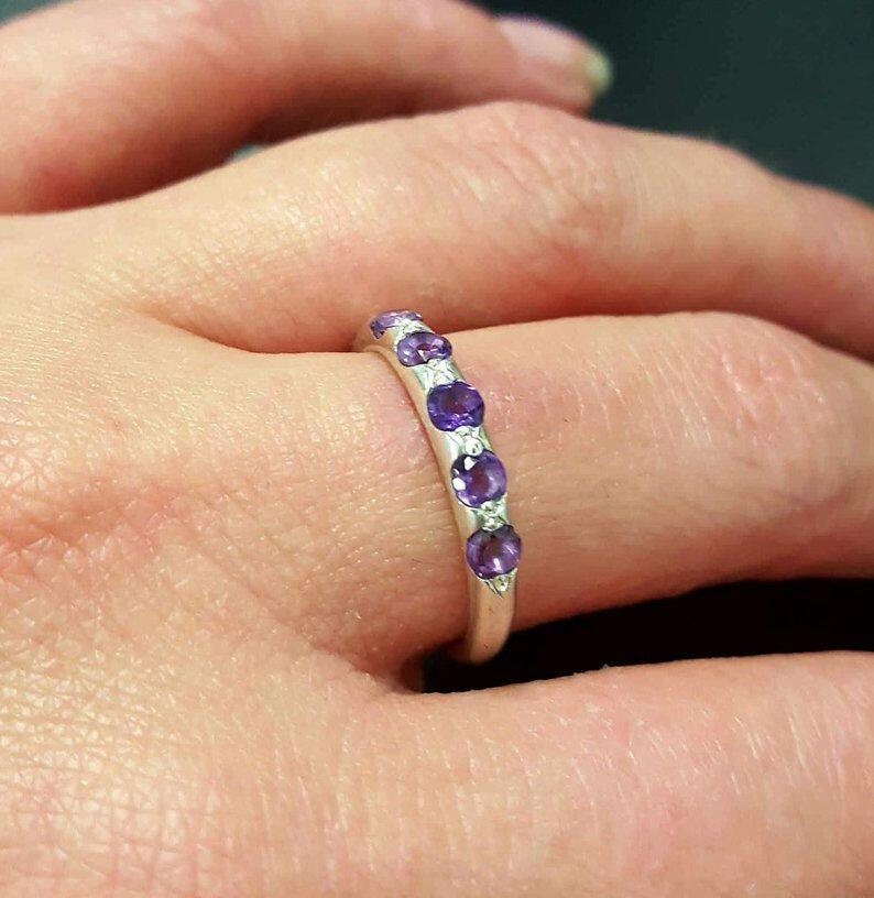 Amethyst Row Eternity Ring worn on ring finger with natural nude nails, dainty silver band featuring sparkling purple gems, perfect for symbolizing calmness and strength, an ideal February birthstone gift, great for birthdays, anniversaries, and evening dinners.