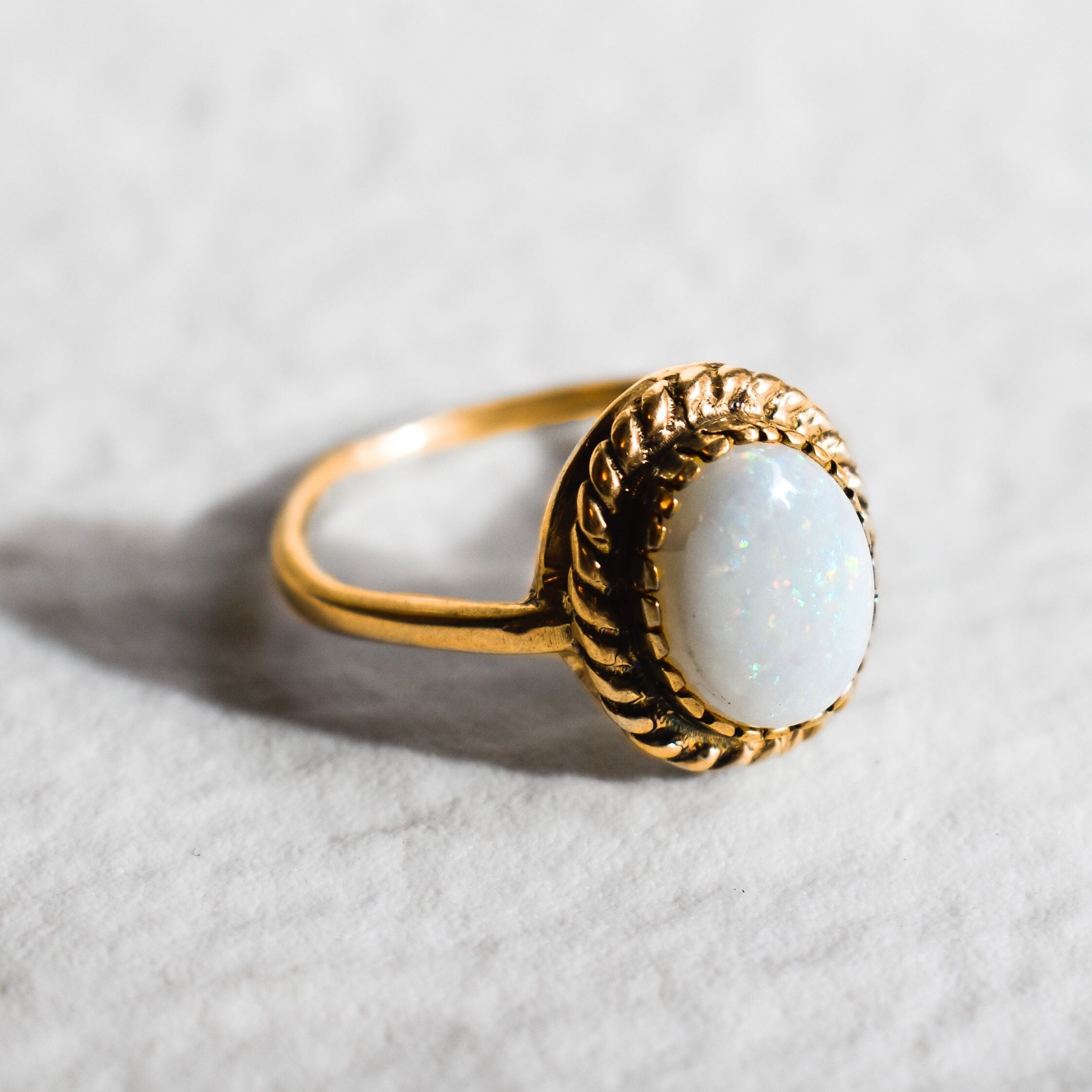 Natural Australian Opal gold ring with an oval cabochon cut gemstone framed by an intricate rope-edge design, offering a classic and elegant style. Opal, the October birthstone, is known for inspiring creativity and emotional harmony, making it an ideal gift for birthdays, anniversaries, weddings, or special celebrations.