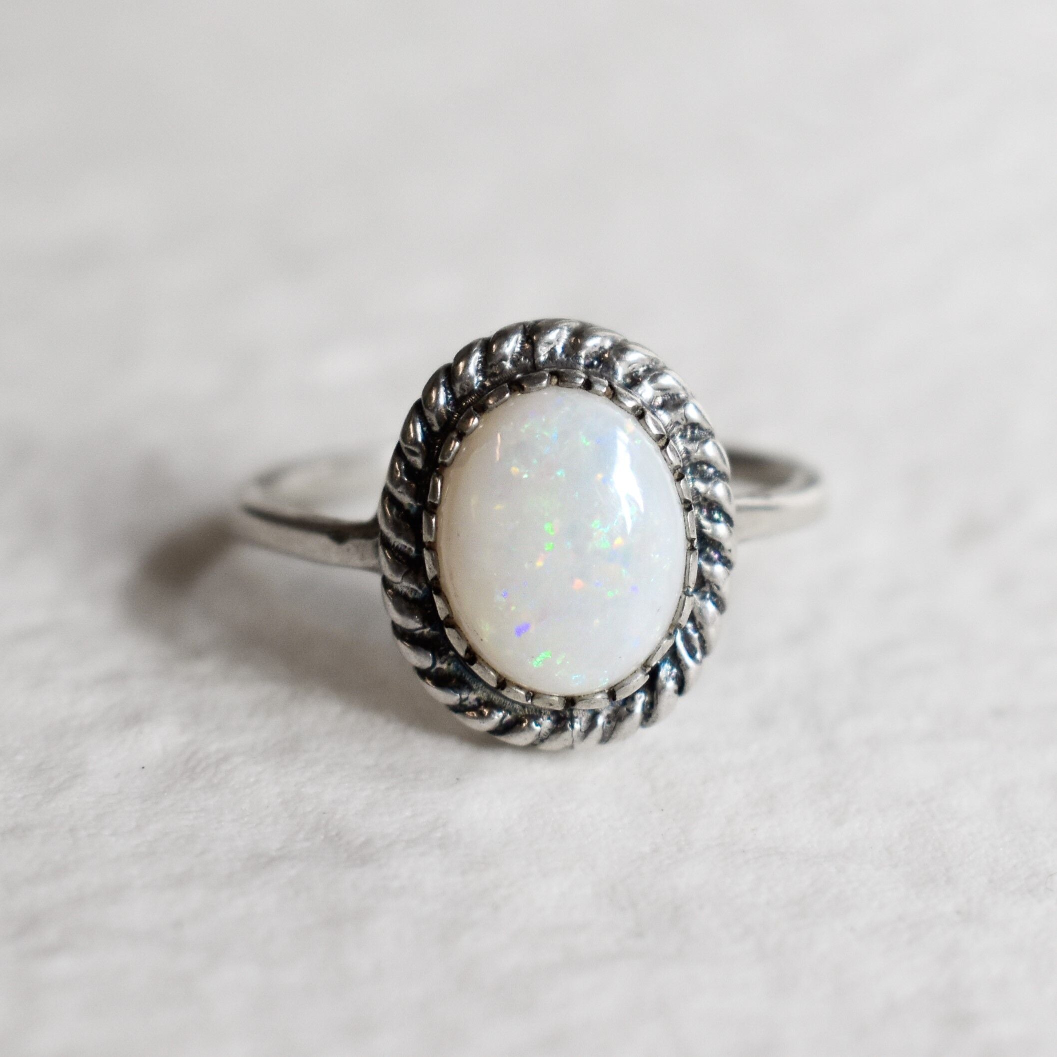 Natural Australian Opal sterling silver ring with an oval cabochon cut gemstone framed by a detailed rope-edge design, offering a timeless and elegant style. Opal, the October birthstone, is valued for enhancing creativity and emotional harmony, making it an ideal gift for birthdays, anniversaries, weddings, and milestone celebrations.