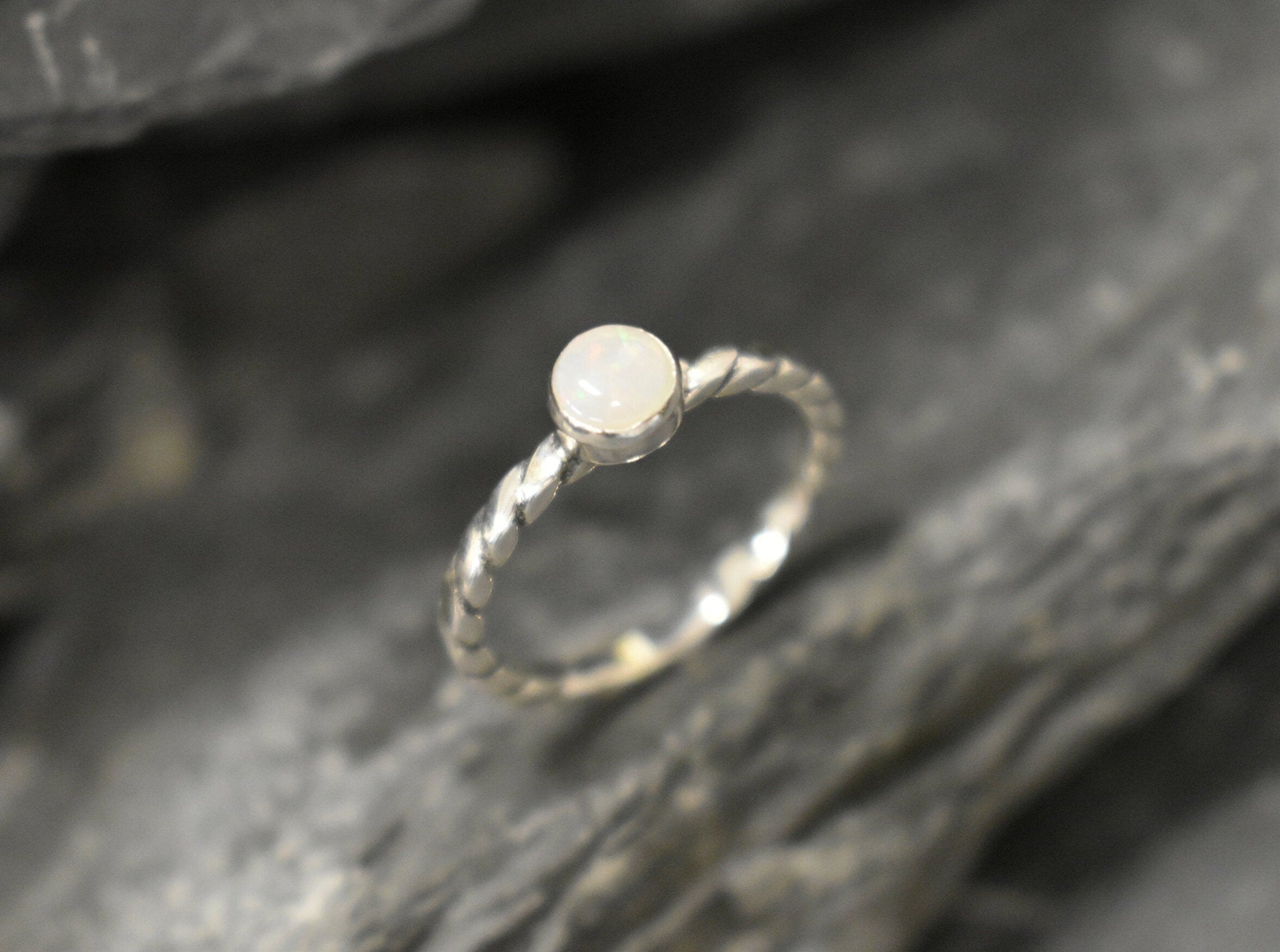 White Opal bezel solitaire ring with round cut stone and twisted band in sterling silver, a timeless jewelry style that highlights flashes of fire colors and durability. Offers the benefit of a secure bezel setting with a refined solitaire look, making it a meaningful October birthstone gift idea. Perfect for birthdays, anniversaries, engagements, and daily wear events.