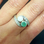 Bypass style ring featuring a natural Green Emerald and a cabochon White Opal in solid 925 sterling silver, accented with CZ pave stones for added brilliance. The combination of real Emerald and Opal highlights vibrant green tones and flashes of fire colors. With Emerald as the May Birthstone and Opal as the October Birthstone, this two stone design makes a meaningful gift for birthdays, anniversaries, and personal milestones. Perfect to wear at weddings, evening parties, and special celebrations.