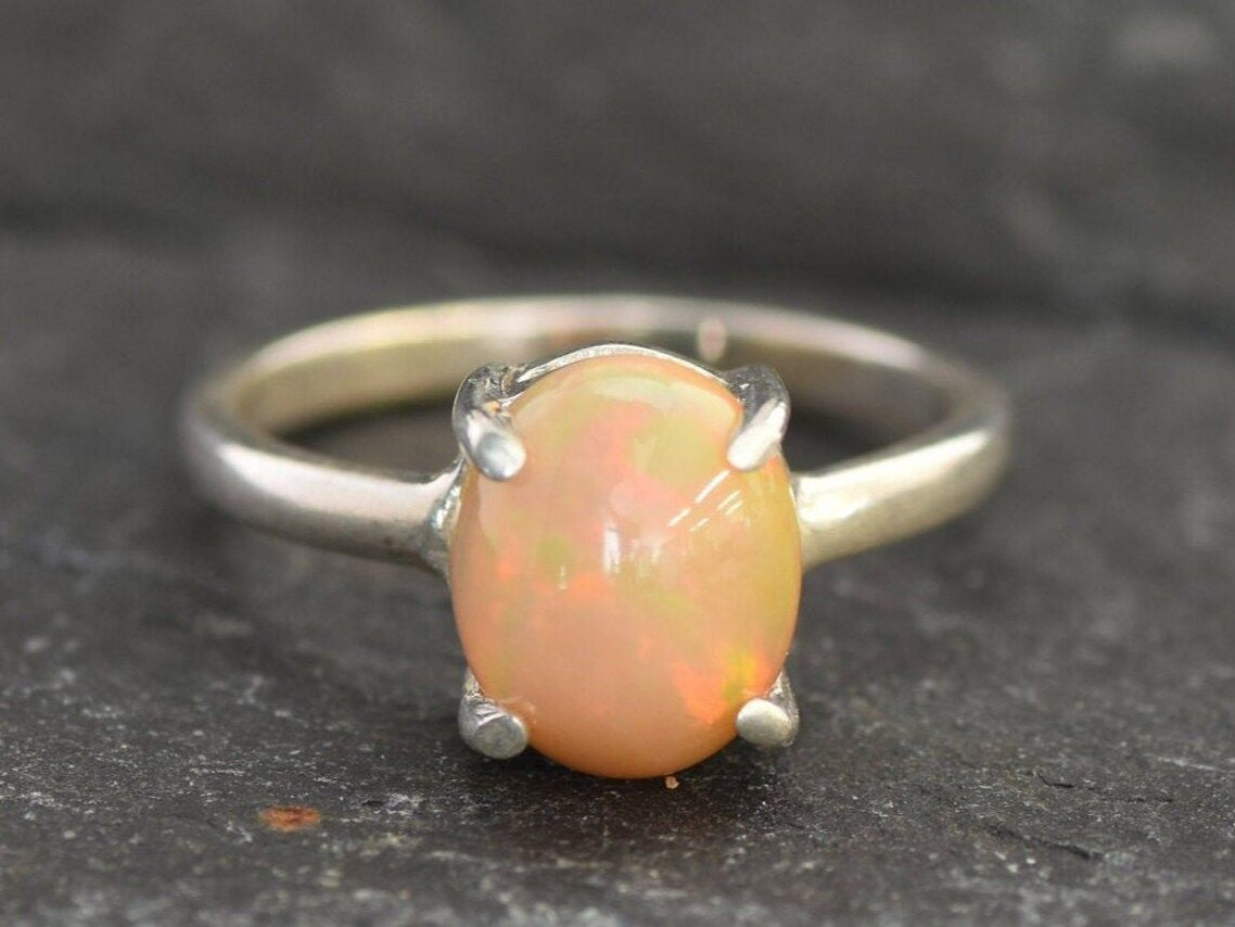 Ethiopian Fire Opal Solitaire Ring in sterling silver with a cabochon cut oval stone showing flashes of fire colors. Opal is linked to creativity, inspiration, and emotional balance, making it a meaningful October birthstone gift. A thoughtful choice for birthdays, anniversaries, promise rings, or engagements. Suitable for daily wear, weddings, and classic elegant occasions.