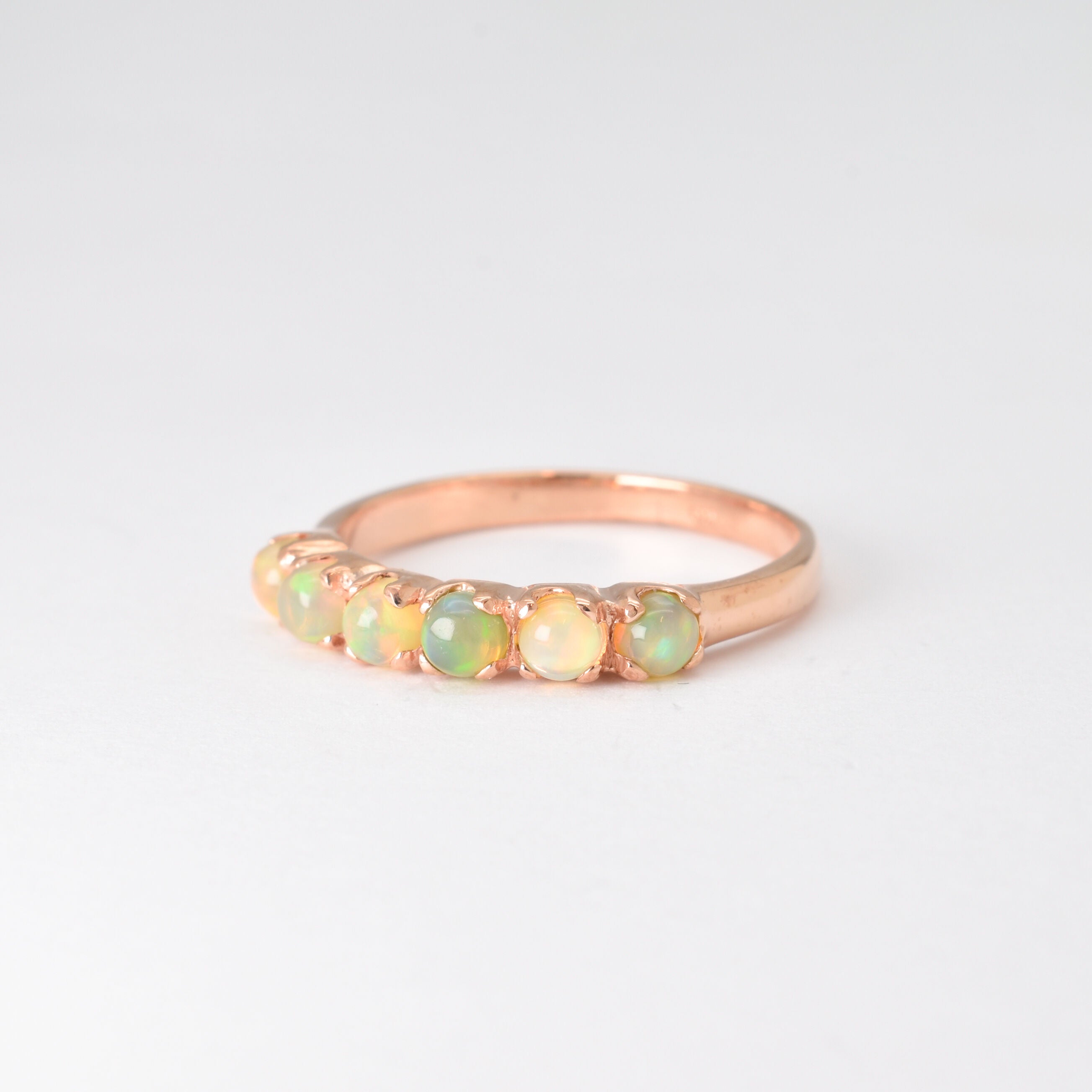 Rose gold half eternity ring with cabochon-cut opals showcasing flashes of fire colors, symbolizing hope and emotional balance, perfect as an October birthstone gift for weddings, anniversaries, or everyday elegance.