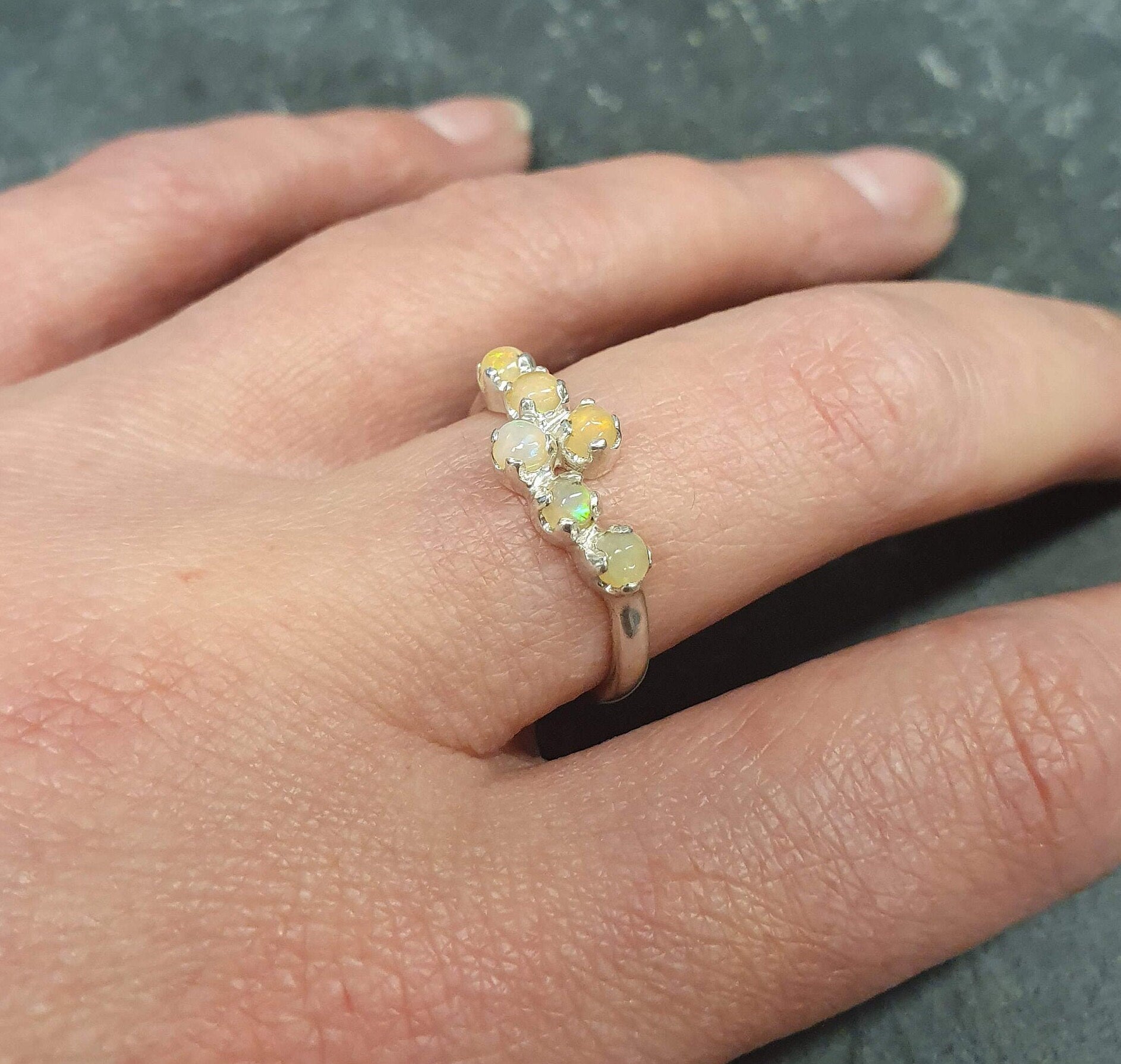 Dainty Fire Opal Cabochon Ring in bypass design worn on index finger with bare nails, glowing with fire colors, styled effortlessly with a black ribbed top, ideal for evening outings, birthday dinners, and festive events.