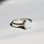 White Opal solitaire ring in sterling silver showcasing flashes of rainbow colors, dainty jewelry style perfect for daily elegance, believed to bring inspiration and emotional balance, a meaningful October birthstone gift idea for anniversaries, engagements, and weddings.