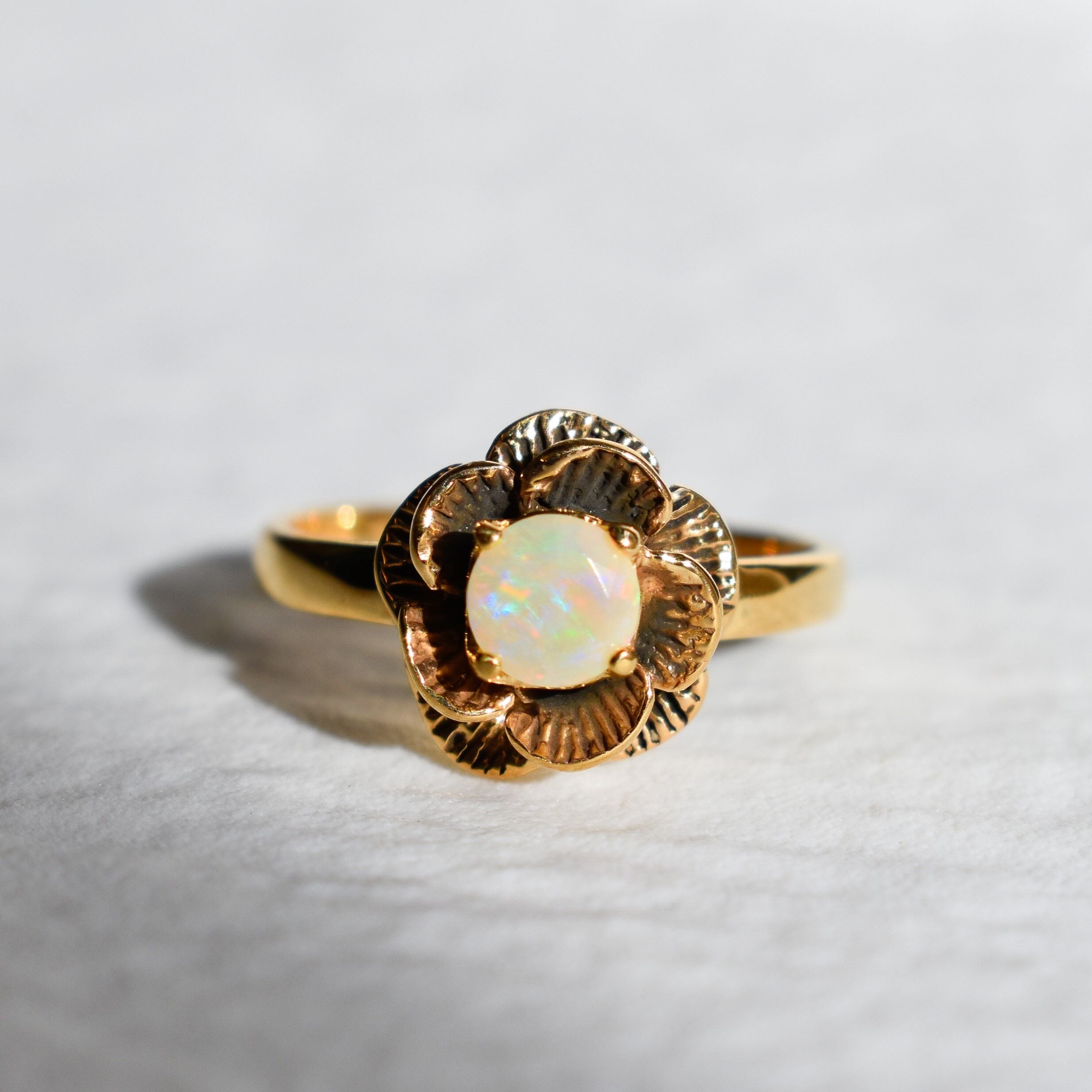 Vintage Fire Opal flower ring with a rose inspired artisan design in gold. The daisy style petals frame a round opal center for a floral and feminine look. Opal is believed to bring hope, creativity and emotional balance, making it a meaningful October birthstone gift. Perfect for weddings, anniversaries, special celebrations and romantic events.