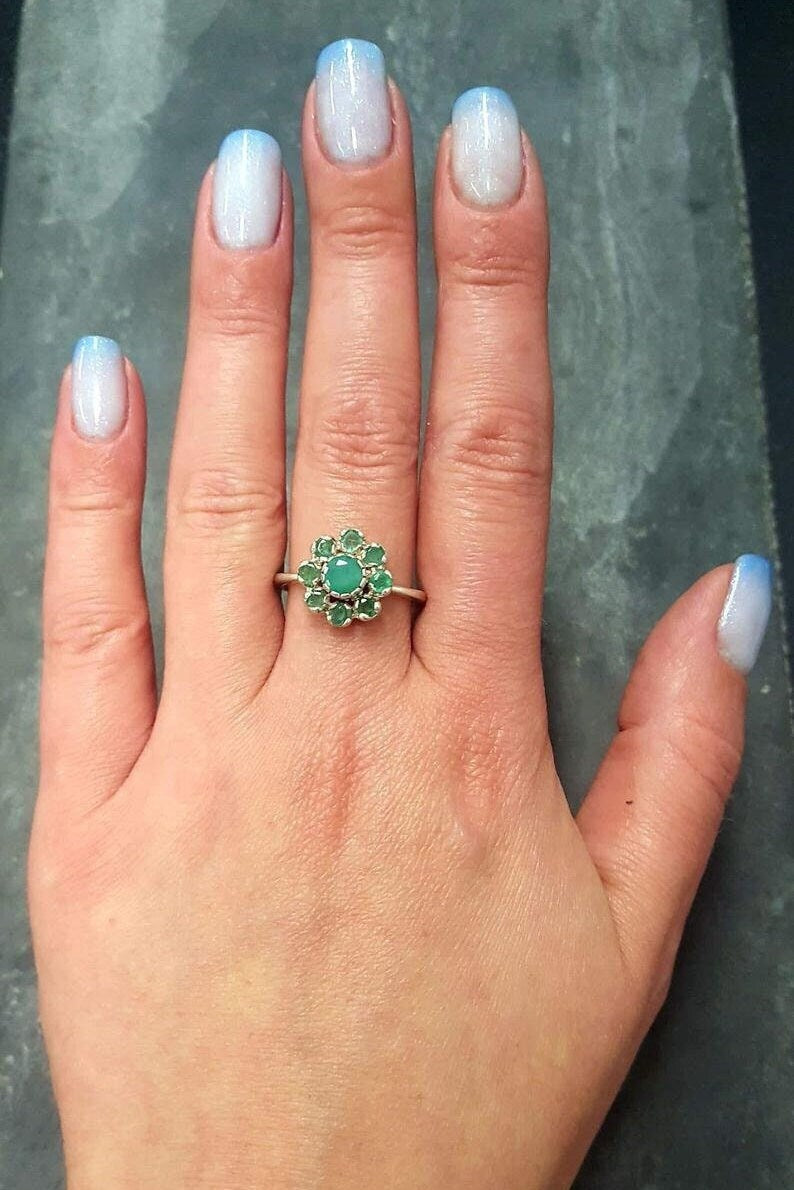 Emerald Flower Ring worn on middle finger with light blue gradient nails. The ring features a floral cluster of genuine emeralds in sterling silver. Emerald is the May birthstone linked to love, harmony, and renewal, making it a meaningful gift for birthdays, anniversaries, or promise occasions. Perfect to wear for weddings, family gatherings, and elegant parties.