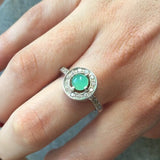 Emerald Halo Ring worn on the index finger with glossy red nails, sterling silver band accented with CZ stones highlighting the central opal’s flashes of fire colors. A chic October Birthstone design perfect for evening parties, romantic dinners, and wedding receptions.