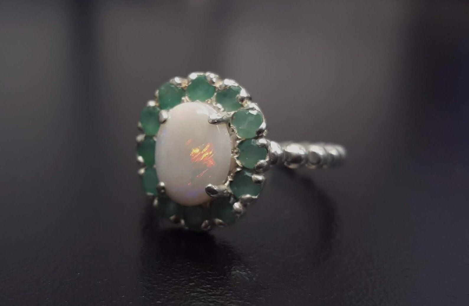 Opal halo floral ring with Genuine Emeralds in a vintage victorian flower halo, White cabochon center, and beaded Bubble Band for a bold statement cocktail look showing flashes of fire colors. Benefits include creativity, harmony, and calm. Ideal October birthstone gift with meaningful May emerald accents.
Worn for weddings, cocktail parties, anniversaries, graduations, garden events, and holiday gatherings.