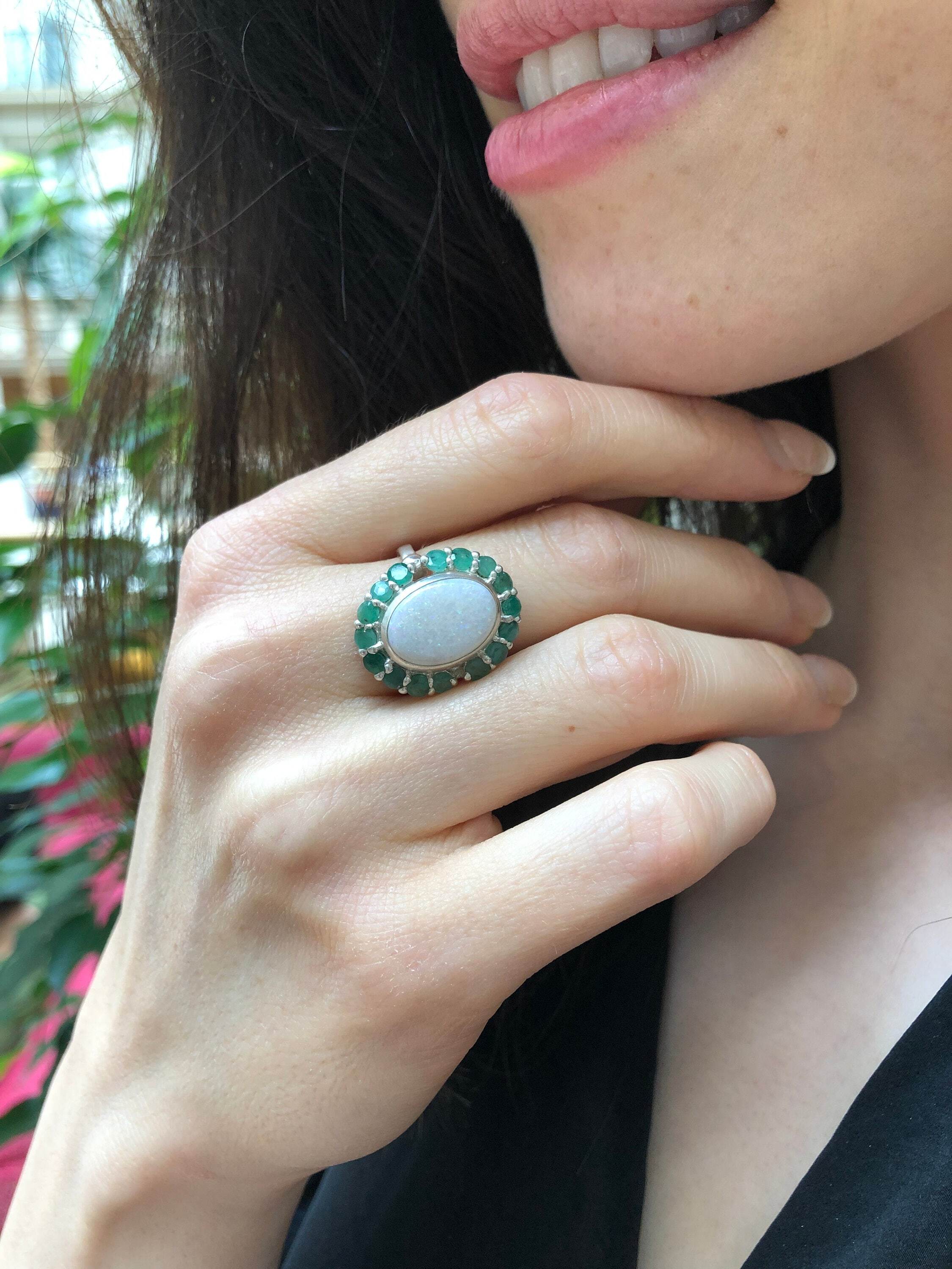 Flower Opal Ring with emerald halo worn on index finger with nude nails, a bold cocktail statement piece that enhances confidence, meaningful as an October and May birthstone gift, perfect for weddings and gala events.