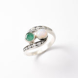 Bypass style ring featuring a natural Green Emerald and a cabochon White Opal in solid 925 sterling silver, accented with CZ pave stones for added brilliance. The combination of real Emerald and Opal highlights vibrant green tones and flashes of fire colors. With Emerald as the May Birthstone and Opal as the October Birthstone, this two stone design makes a meaningful gift for birthdays, anniversaries, and personal milestones. Perfect to wear at weddings, evening parties, and special celebrations.