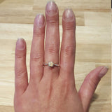 Fire Opal Engagement Ring styled on hand with short nude nails. The round solitaire opal glows with flashes of fire colors on a simple silver band. A thoughtful October birthstone gift and a meaningful choice for a promise ring. Perfect for engagements, weddings, or everyday elegance.