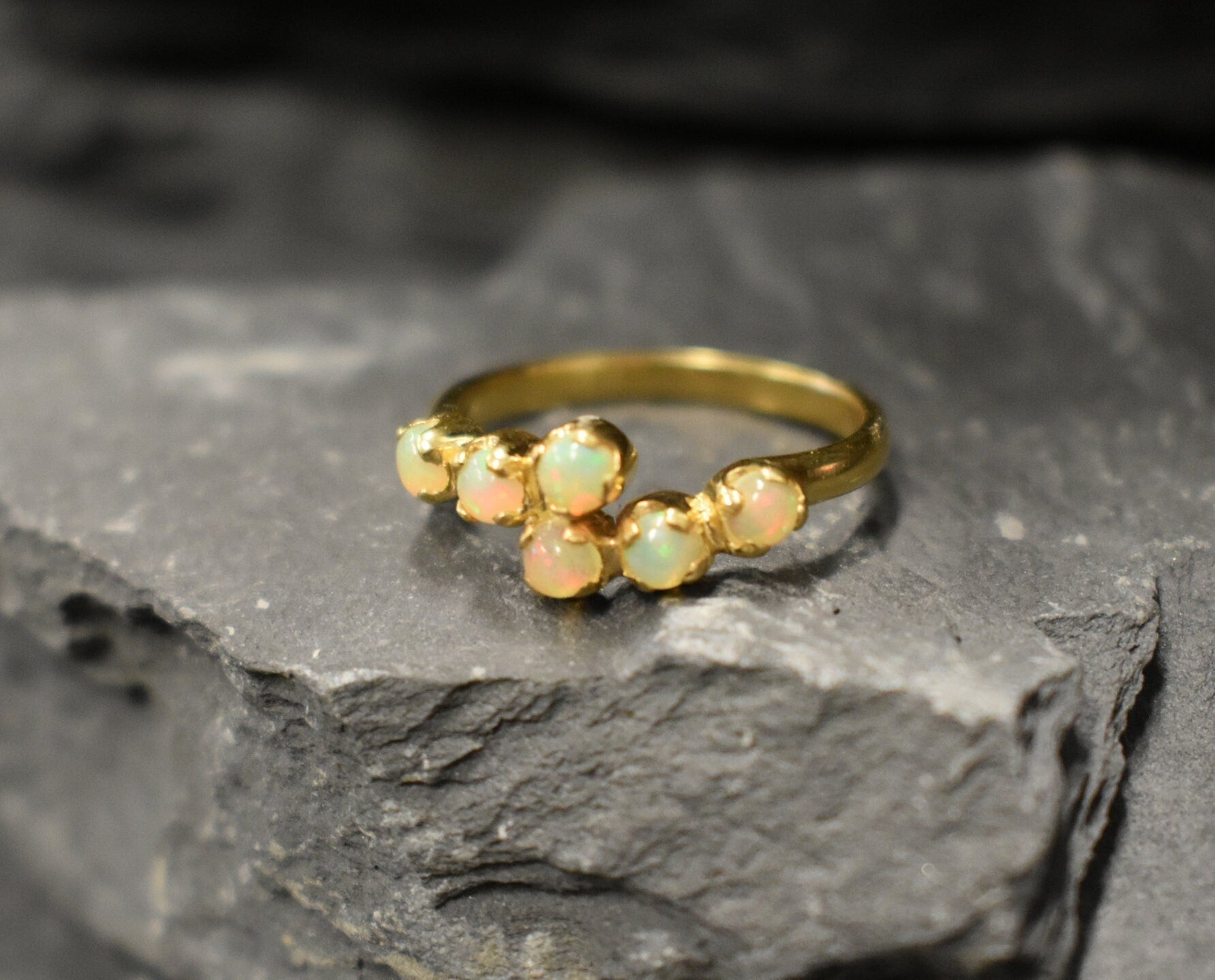 Ethiopian Opal Bypass Ring in gold with six cabochon stones aligned in a curved wrap setting, a stylish jewelry design that radiates flashes of fire colors and adds a modern edge, making it a thoughtful October birthstone gift idea. Perfect to wear at weddings, cocktail parties, and romantic dinners for a bold yet refined look.