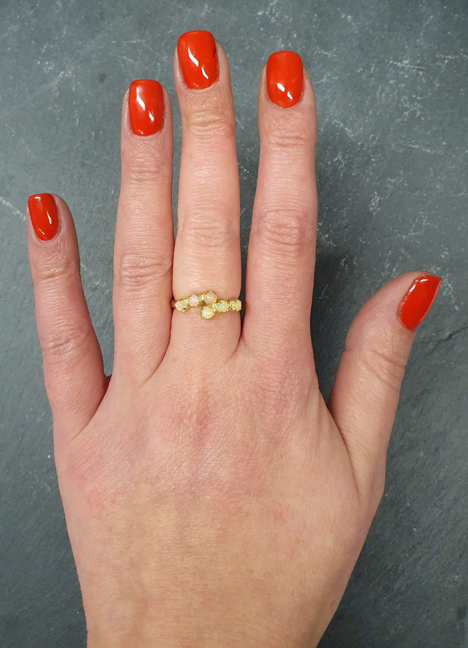 Flower Opal Ring worn on middle finger with natural nails, crafted with six cabochon stones in a curved bypass band, symbolic as an October birthstone gift, ideal for anniversaries and elegant dinner dates.