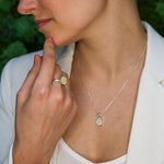 Ethiopian Opal Ring worn on middle finger with pink nails and matching Ethiopian Opal Pendant Necklace styled with a white blazer. The cabochon cut opals show flashes of fire colors set in sterling silver. A classic and elegant jewelry set perfect for October birthstone gifting, anniversaries, promise occasions, and formal events.