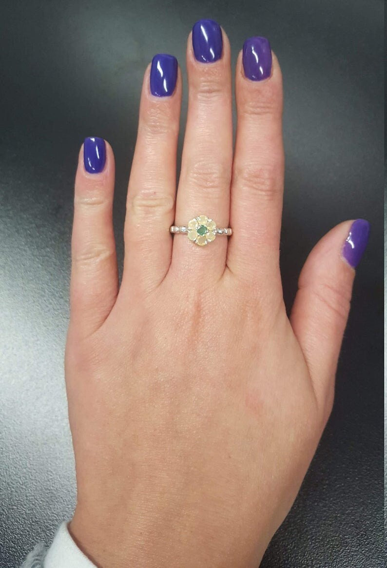 Fire Opal Flower Ring styled on middle finger with deep purple nail polish, showcasing its flashes of fire colors against the sterling silver bubble band. Known for uplifting moods and inspiring originality, this October birthstone gift idea is a nature-inspired treasure. Perfect for autumn weddings, evening soirées, and milestone celebrations.