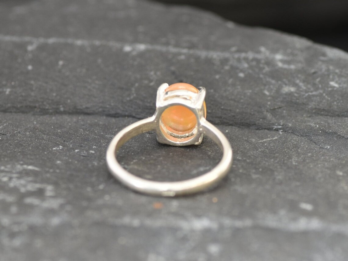 Ethiopian Fire Opal Solitaire Ring in sterling silver with a cabochon cut oval stone showing flashes of fire colors. Opal is linked to creativity, inspiration, and emotional balance, making it a meaningful October birthstone gift. A thoughtful choice for birthdays, anniversaries, promise rings, or engagements. Suitable for daily wear, weddings, and classic elegant occasions.