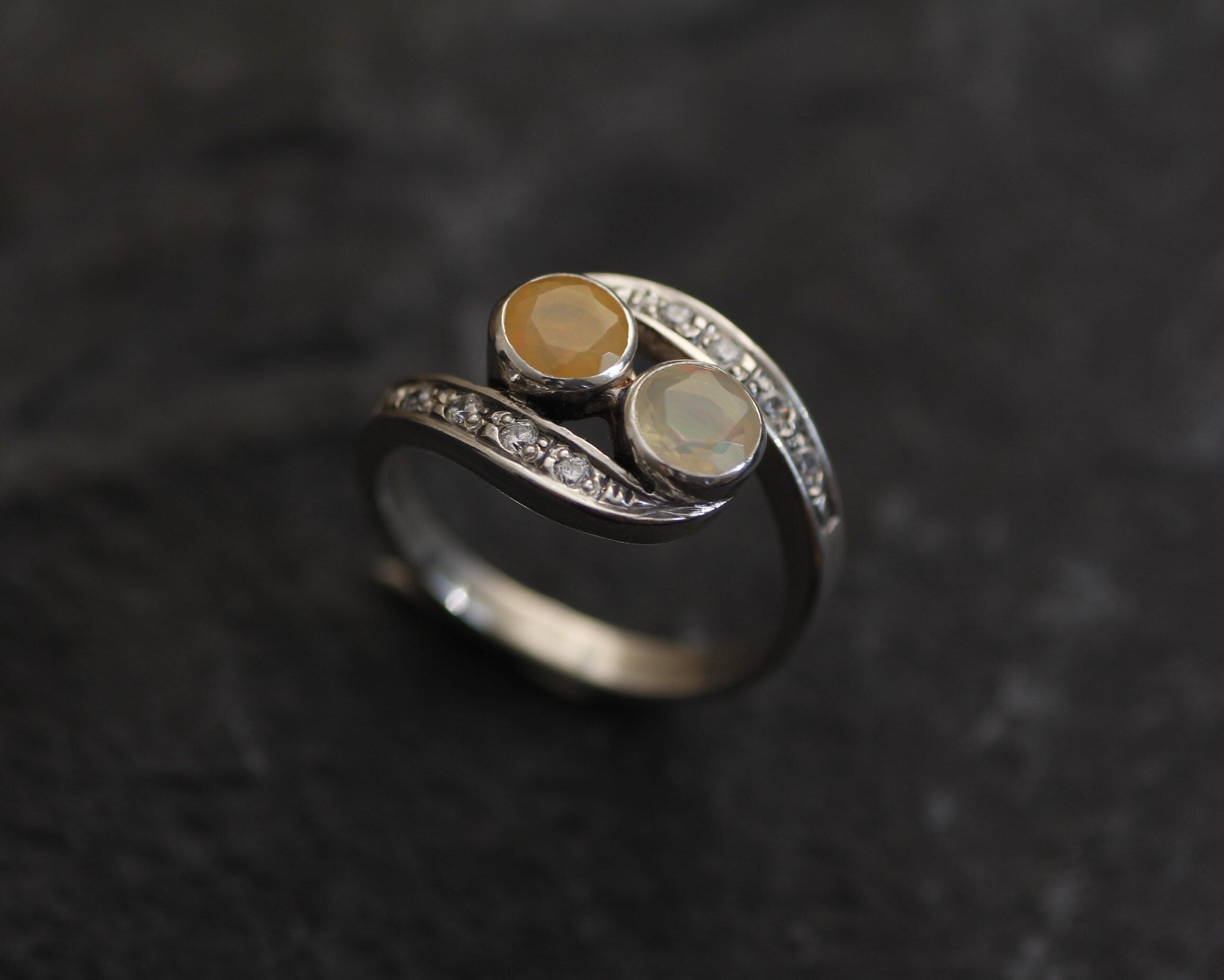 Two-Stone Opal Bypass Wave Ring in sterling silver showcasing cabochon-cut opals with flashes of fire colors and CZ pave accents for an elegant jewelry style. Known for enhancing emotional clarity and balance, this October birthstone ring makes a thoughtful and meaningful gift idea. Perfect for anniversaries, weddings, cocktail events, and celebratory occasions where sophistication shines.