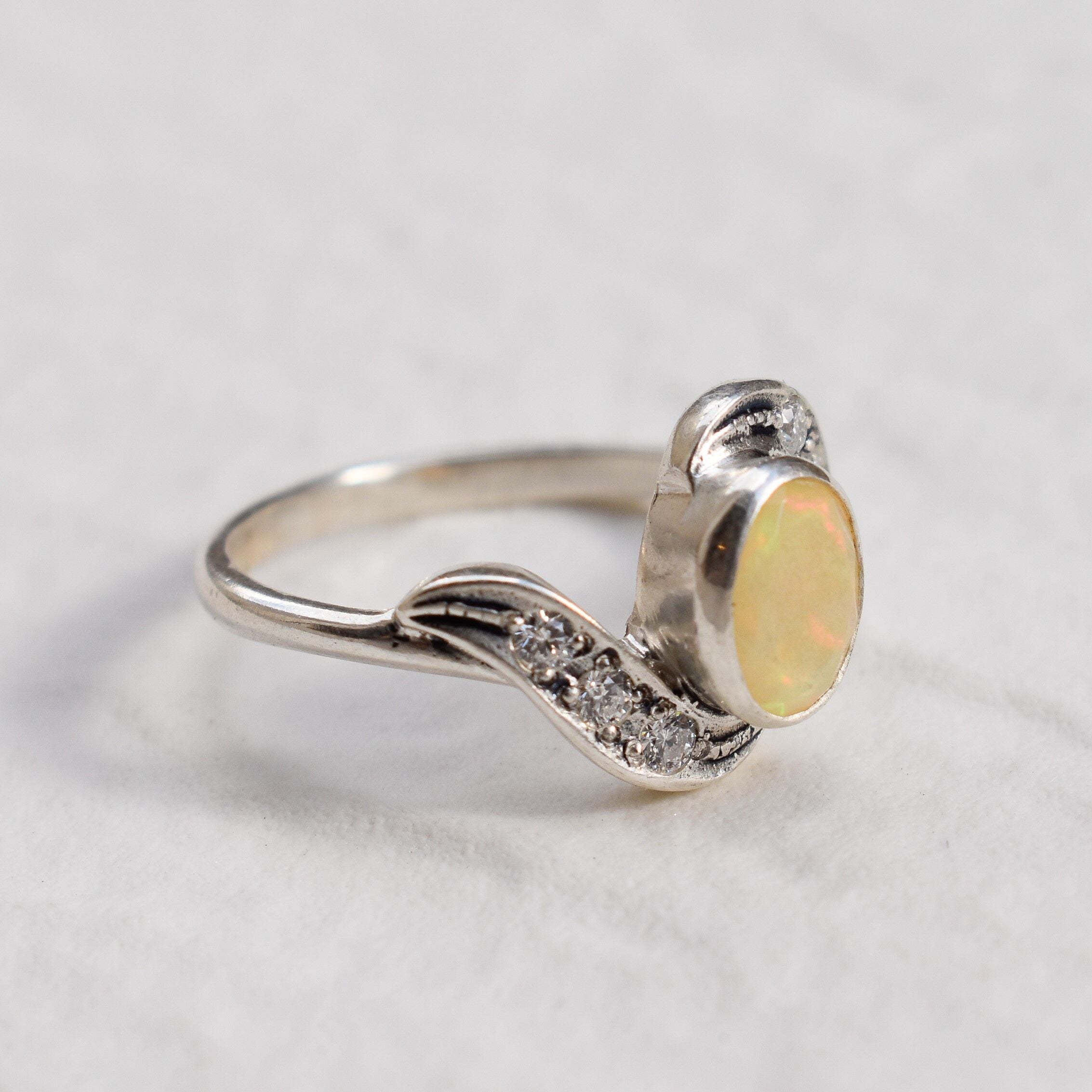 Fire Opal bezel wave ring with CZ pave in sterling silver, featuring flashes of rainbow fire colors, designed in a dainty jewelry style symbolizing passion and hope, a powerful October birthstone gift idea for engagements, anniversaries, and special occasions.