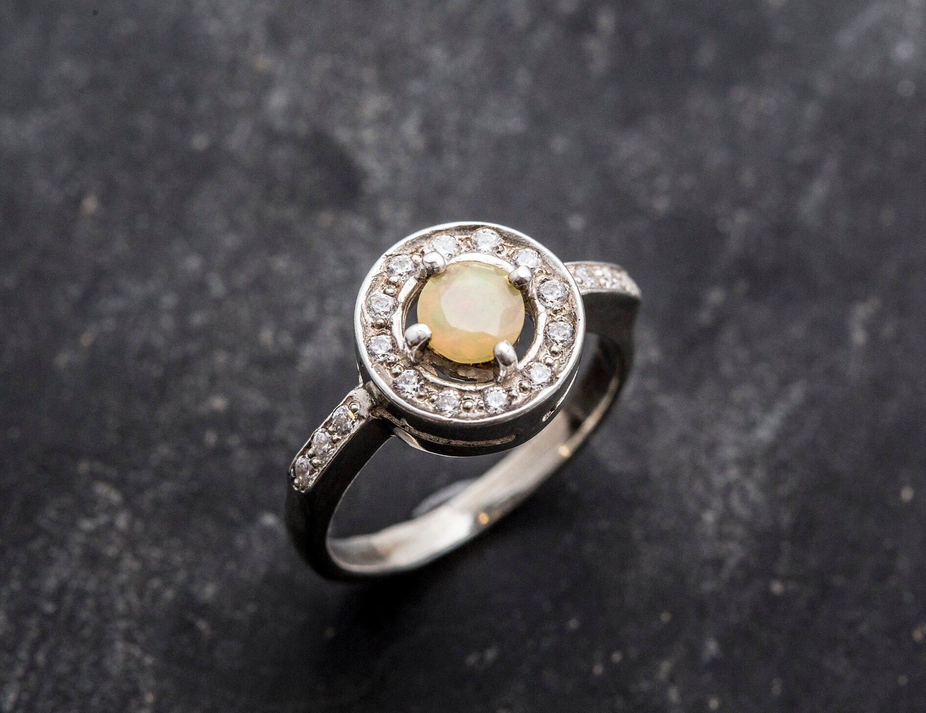 Ethiopian Opal diamond cut halo ring in solid 925 sterling silver, surrounded by sparkling CZ accents for brilliance and elegance. The halo design highlights flashes of fire colors while offering timeless durability. As the October Birthstone, Opal makes a meaningful gift for birthdays, engagements, anniversaries, or personal milestones. Perfect to wear at weddings, cocktail parties, and festive gatherings.