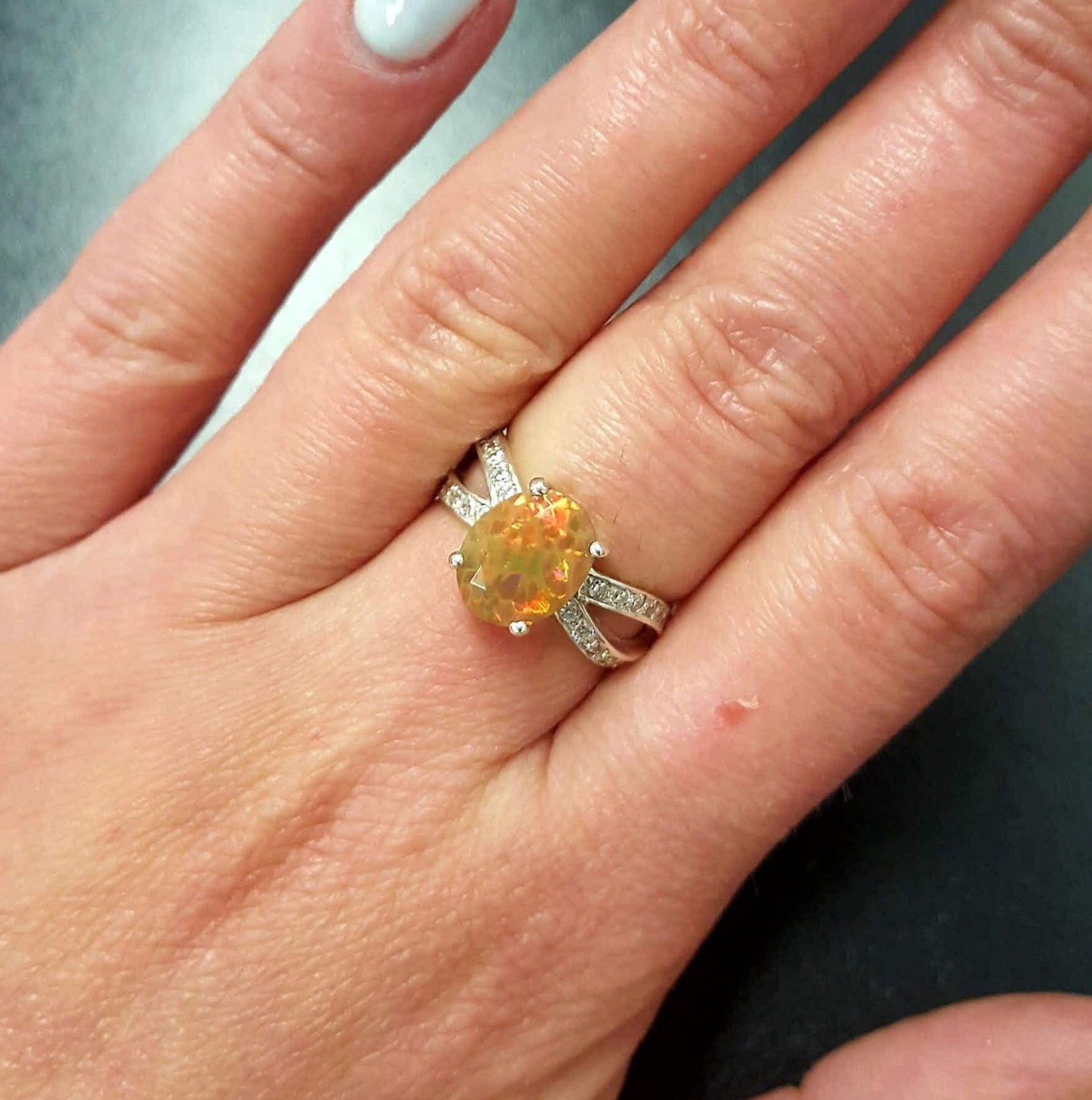 Opal Oval Ring worn on middle finger with natural nails. Jewelry style is bold and refined with a split shank band and 4 prong setting. The gemstone shows flashes of fire colors with added sparkle from the CZ pave band. Brings creativity, inspiration, and balance. A thoughtful birthstone gift for October birthdays and anniversaries. Ideal for weddings, family gatherings, and formal dinners.