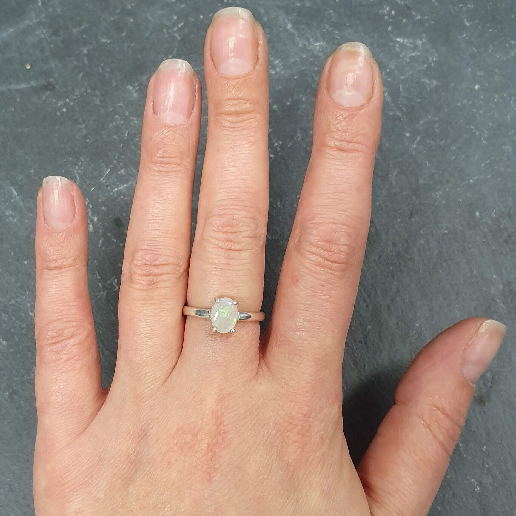 White Opal solitaire ring in sterling silver showcasing flashes of rainbow colors, dainty jewelry style perfect for daily elegance, believed to bring inspiration and emotional balance, a meaningful October birthstone gift idea for anniversaries, engagements, and weddings.