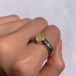 Fire Opal Ring worn on the middle finger with nude nails, engraved tribal ornament band highlighting its flashes of fire colors. A bold October Birthstone jewelry piece perfect for music festivals, boho outfits, and casual day events.