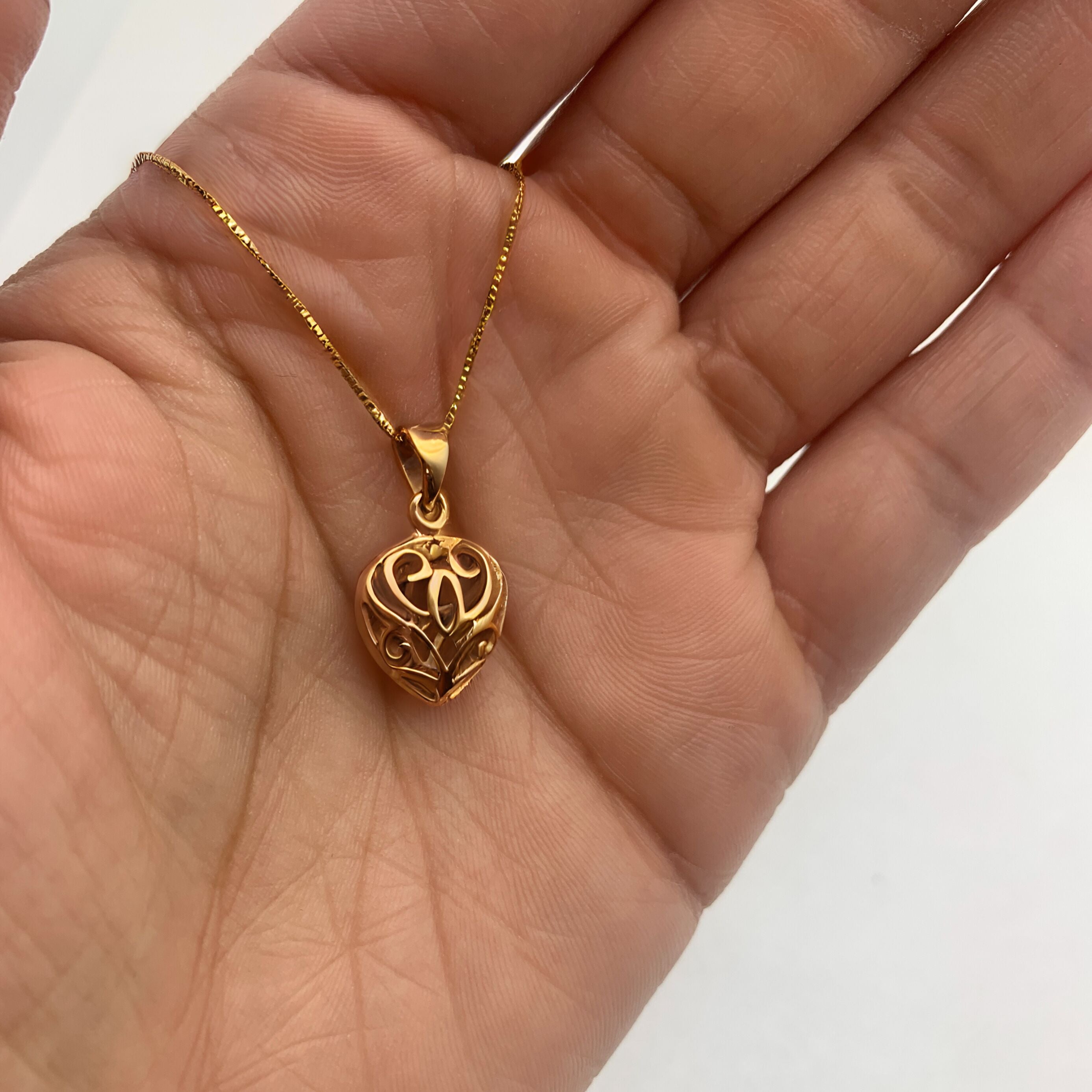 Heart charm necklace in 18k yellow gold over sterling silver, resting in an open palm - puffed heart pendant for size reference. 