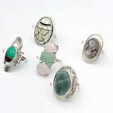 Picture of five rings: Mosaic lady ring made of mother of pearl, carved lady cameo ring, chrysoprase metrix ring, three stone ring with rose quartz and jade, and seraphinite ring