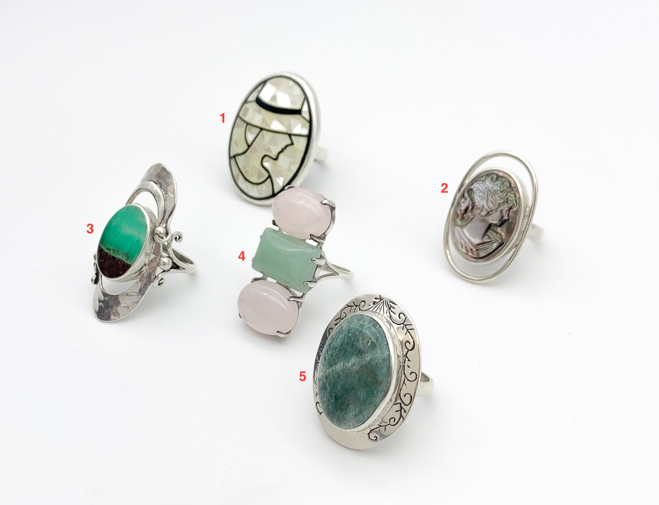 Picture of five rings: Mosaic lady ring made of mother of pearl, carved lady cameo ring, chrysoprase metrix ring, three stone ring with rose quartz and jade, and seraphinite ring