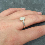 Dainty Opal Engagement Ring styled on middle finger with natural nude nails, ideal for minimalist outfits, believed to inspire creativity and joy, perfect for anniversaries and intimate occasions.