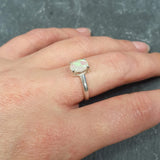 Dainty Opal Engagement Ring styled on middle finger with natural nude nails, ideal for minimalist outfits, believed to inspire creativity and joy, perfect for anniversaries and intimate occasions.