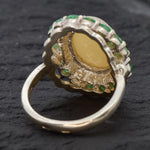 Opal and Emerald Large Cocktail Ring in sterling silver featuring an oval white opal cabochon framed with genuine emerald petals, a statement jewelry style that radiates flashes of fire colors while symbolizing love and renewal, making it a meaningful October and May birthstone gift idea. Perfect for weddings, cocktail parties, and formal evening events where a bold elegant look is desired.