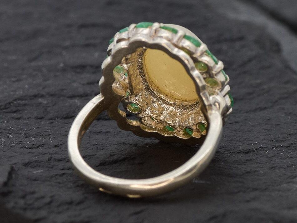 Opal and Emerald Large Cocktail Ring in sterling silver featuring an oval white opal cabochon framed with genuine emerald petals, a statement jewelry style that radiates flashes of fire colors while symbolizing love and renewal, making it a meaningful October and May birthstone gift idea. Perfect for weddings, cocktail parties, and formal evening events where a bold elegant look is desired.
