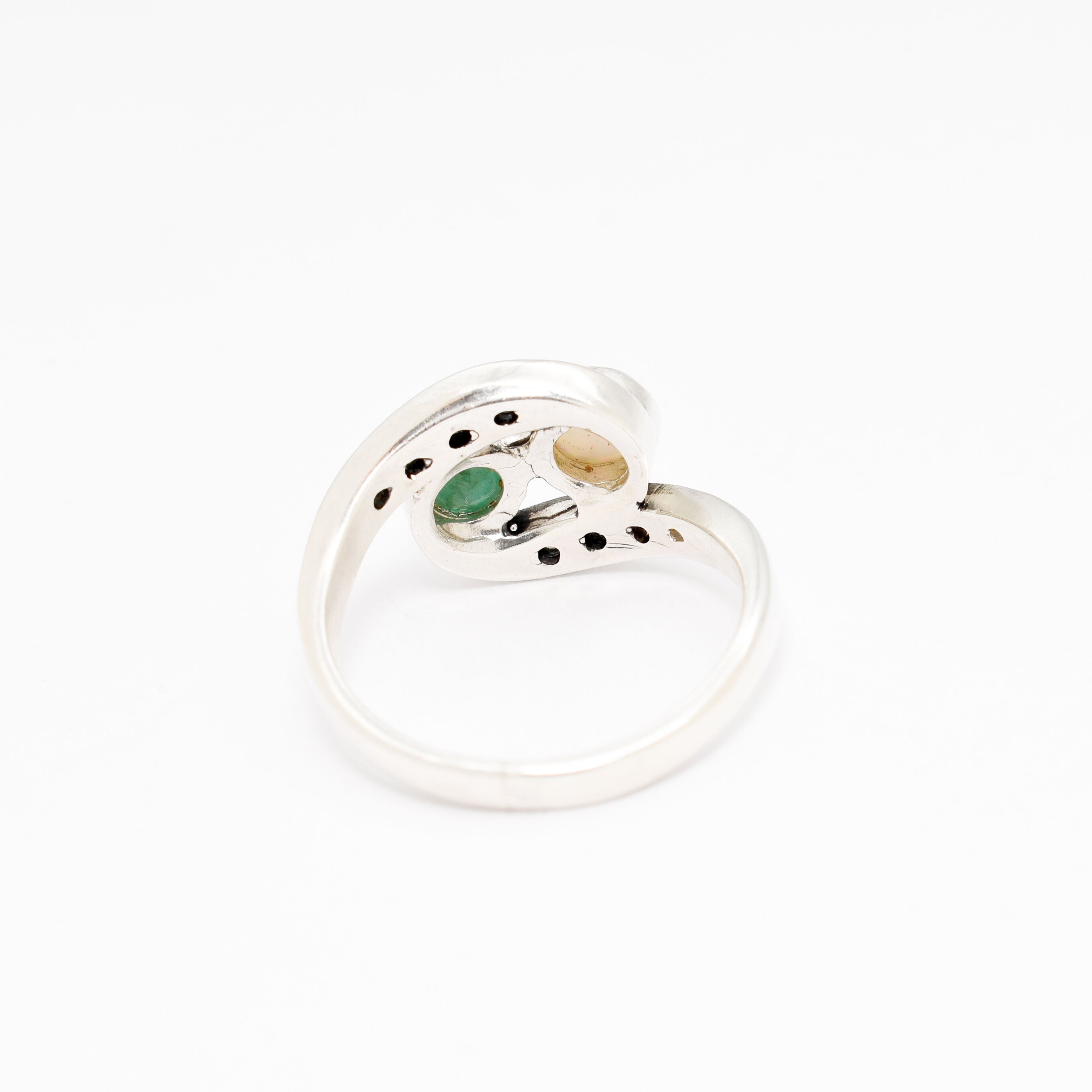 Bypass style ring featuring a natural Green Emerald and a cabochon White Opal in solid 925 sterling silver, accented with CZ pave stones for added brilliance. The combination of real Emerald and Opal highlights vibrant green tones and flashes of fire colors. With Emerald as the May Birthstone and Opal as the October Birthstone, this two stone design makes a meaningful gift for birthdays, anniversaries, and personal milestones. Perfect to wear at weddings, evening parties, and special celebrations.