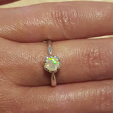 Fire Opal Promise Ring worn on middle finger with natural nails. The dainty round solitaire design shows flashes of fire colors, symbolizing joy and passion. A perfect October birthstone gift for birthdays and anniversaries. Ideal for engagements, weddings, and romantic dinners.
