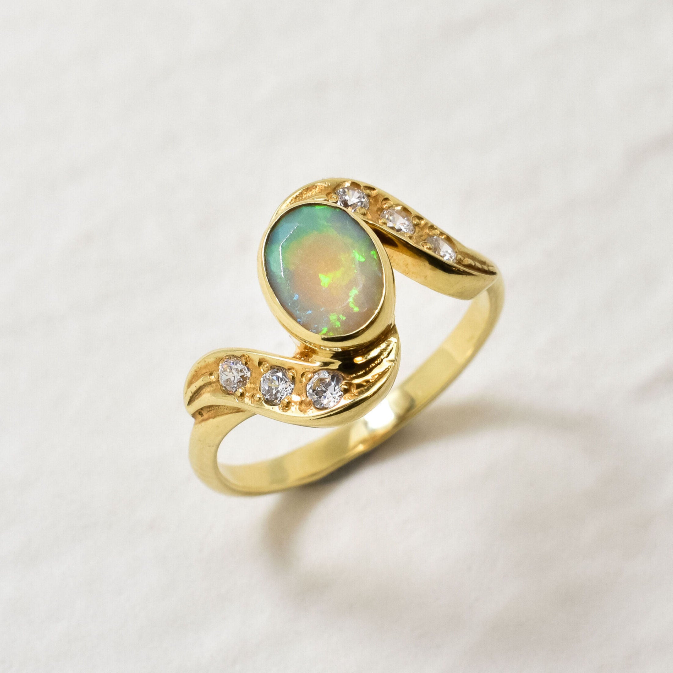 Fire Opal bezel wave ring with CZ pave in gold, featuring flashes of rainbow fire colors, designed in a dainty jewelry style symbolizing passion and hope, a powerful October birthstone gift idea for engagements, anniversaries, and special occasions.