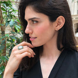 Flower Opal Ring with white opal cabochon styled on middle finger with bare nails, accented by genuine emerald petals for a chic look, symbolic as an October and May birthstone gift, ideal for anniversary dinners and evening celebrations.