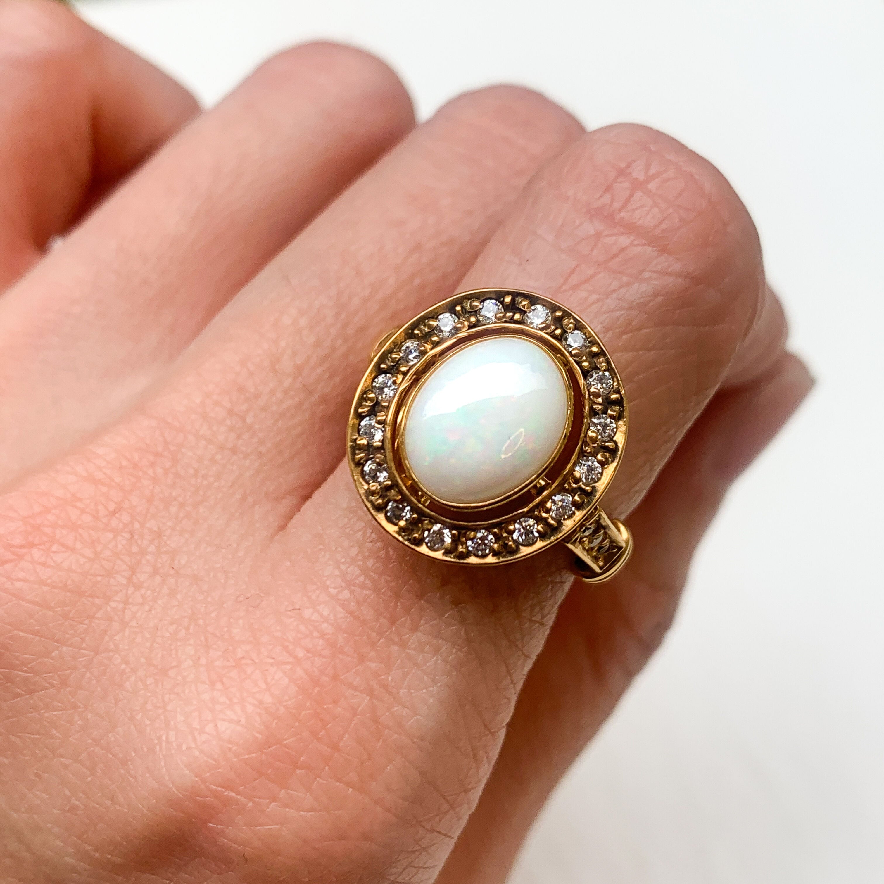 Natural Opal ring in gold with a halo of sparkling diamonds, featuring a cabochon cut gemstone for an elegant and timeless style. Known for promoting creativity and emotional balance, Opal is the October birthstone and makes a thoughtful gift for birthdays, anniversaries, weddings, or milestone celebrations.