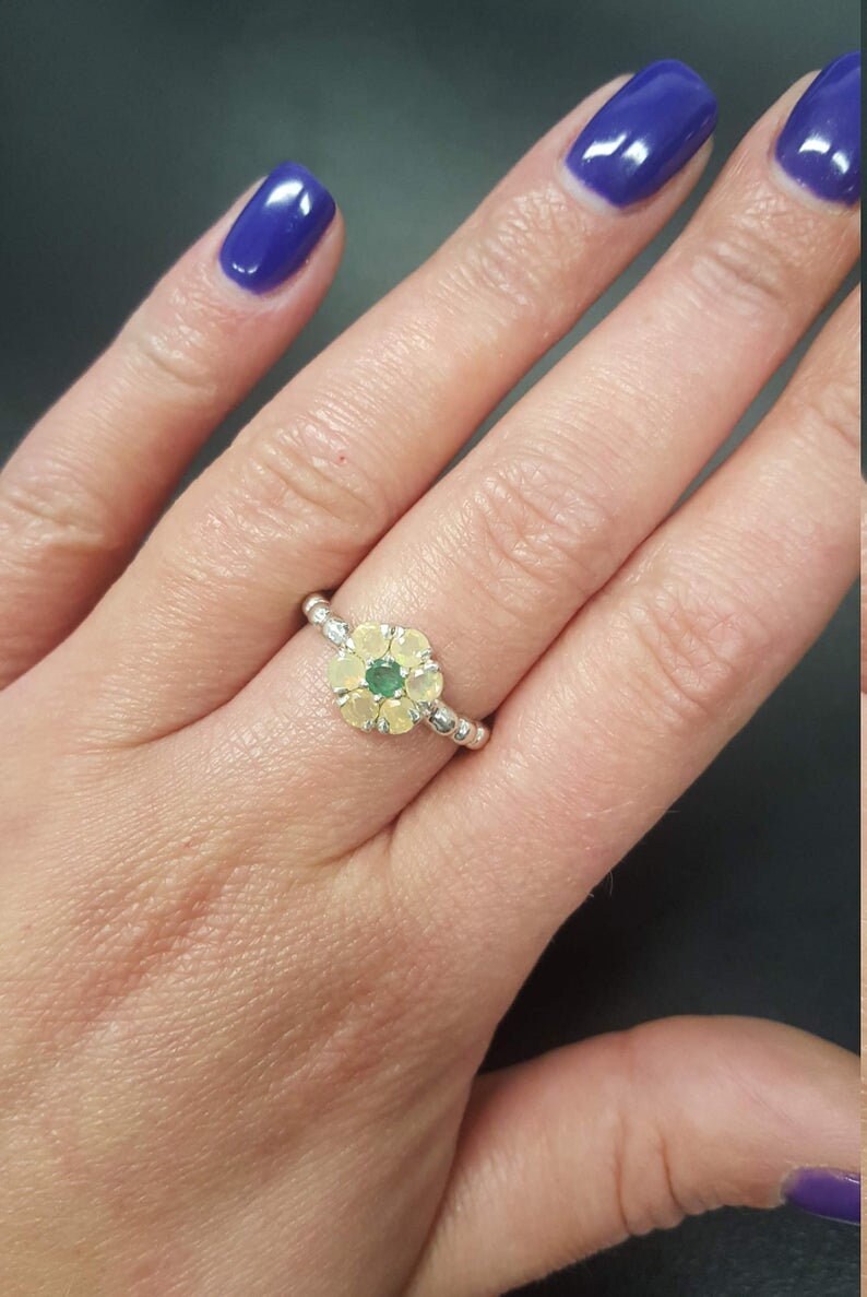 Dainty Flower Opal Ring placed on middle finger with deep purple nails, highlighting its nature-lover daisy design in sterling silver. This October birthstone radiates warmth and creativity, making it a thoughtful gift for loved ones. Best suited for art gallery visits, seasonal parties, and romantic outings.