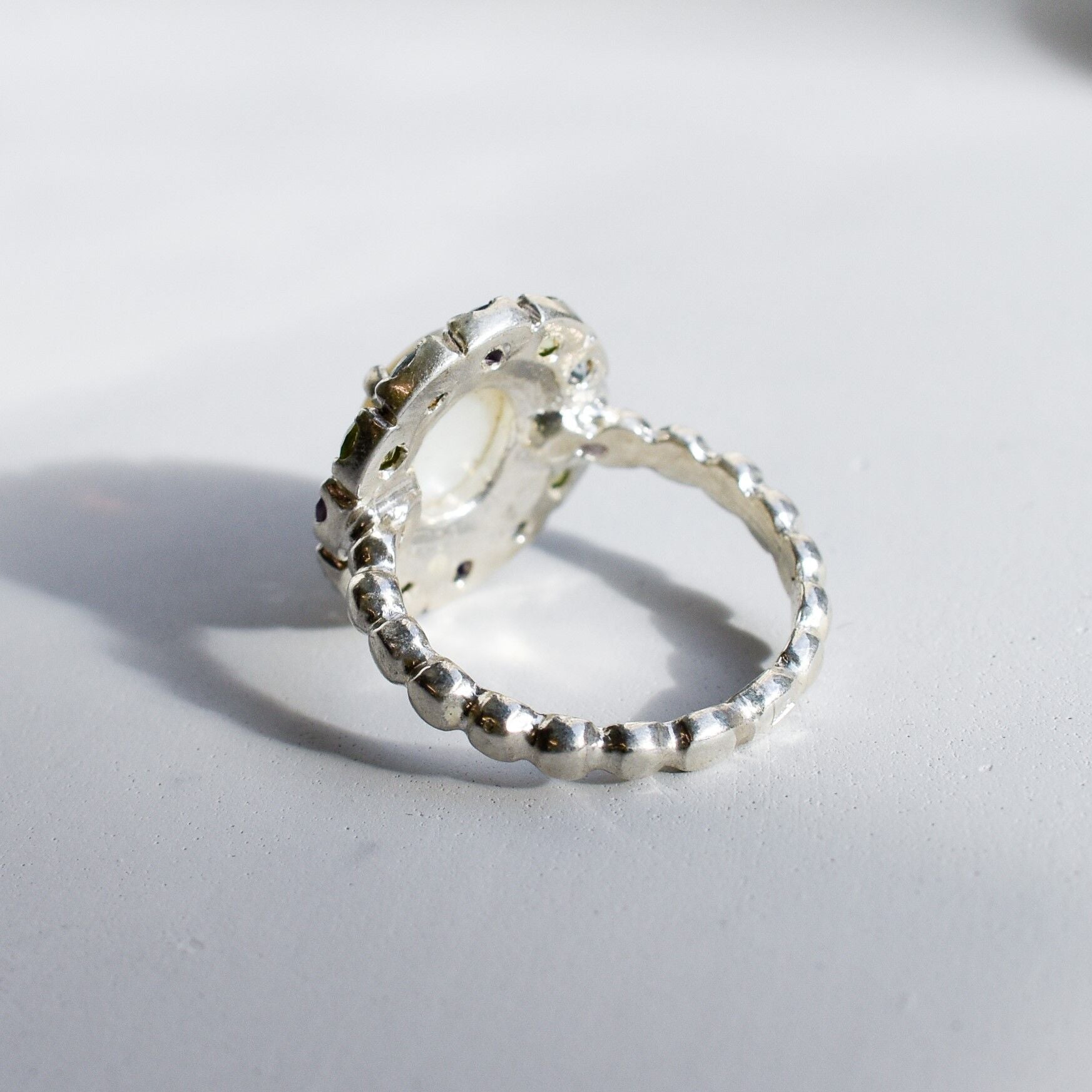 White Opal flower cluster ring in sterling silver with colorful Amethyst and Peridot halo in a cocktail style. The elegant cluster design adds sparkle. Opal is linked with hope and clarity, Amethyst with calm, Peridot with fresh energy. A lovely birthstone gift for October, February and August. Wear to weddings, graduations, dinner dates and holiday parties.