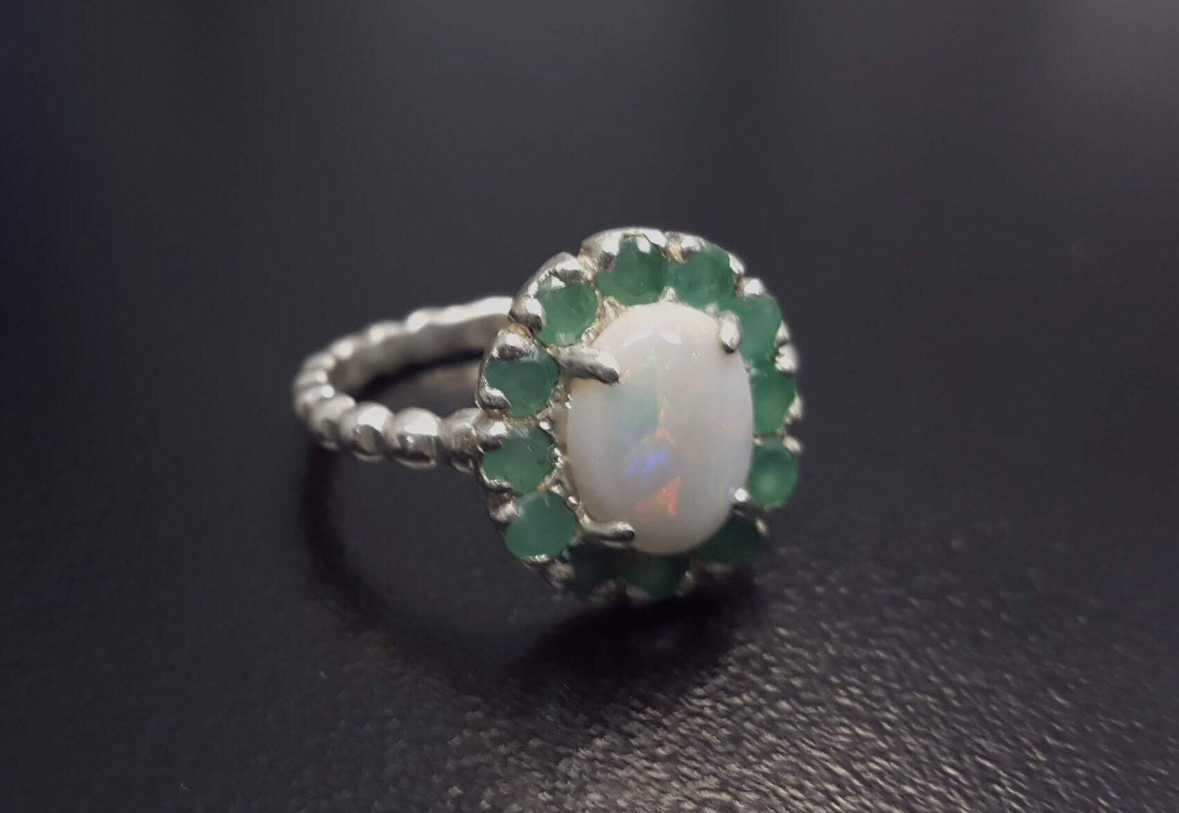 Opal halo floral ring with Genuine Emeralds in a vintage victorian flower halo, White cabochon center, and beaded Bubble Band for a bold statement cocktail look showing flashes of fire colors. Benefits include creativity, harmony, and calm. Ideal October birthstone gift with meaningful May emerald accents.
Worn for weddings, cocktail parties, anniversaries, graduations, garden events, and holiday gatherings.