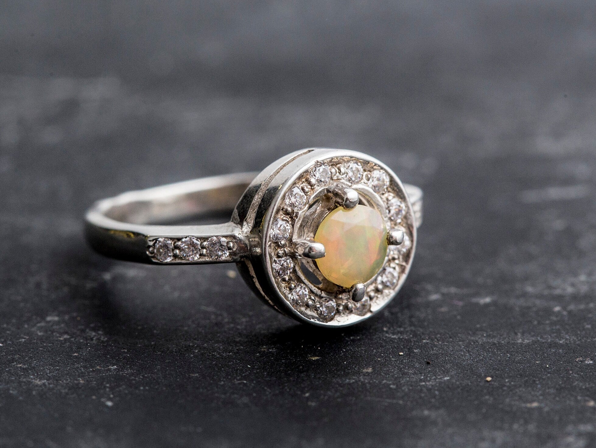 Ethiopian Opal diamond cut halo ring in solid 925 sterling silver, surrounded by sparkling CZ accents for brilliance and elegance. The halo design highlights flashes of fire colors while offering timeless durability. As the October Birthstone, Opal makes a meaningful gift for birthdays, engagements, anniversaries, or personal milestones. Perfect to wear at weddings, cocktail parties, and festive gatherings.