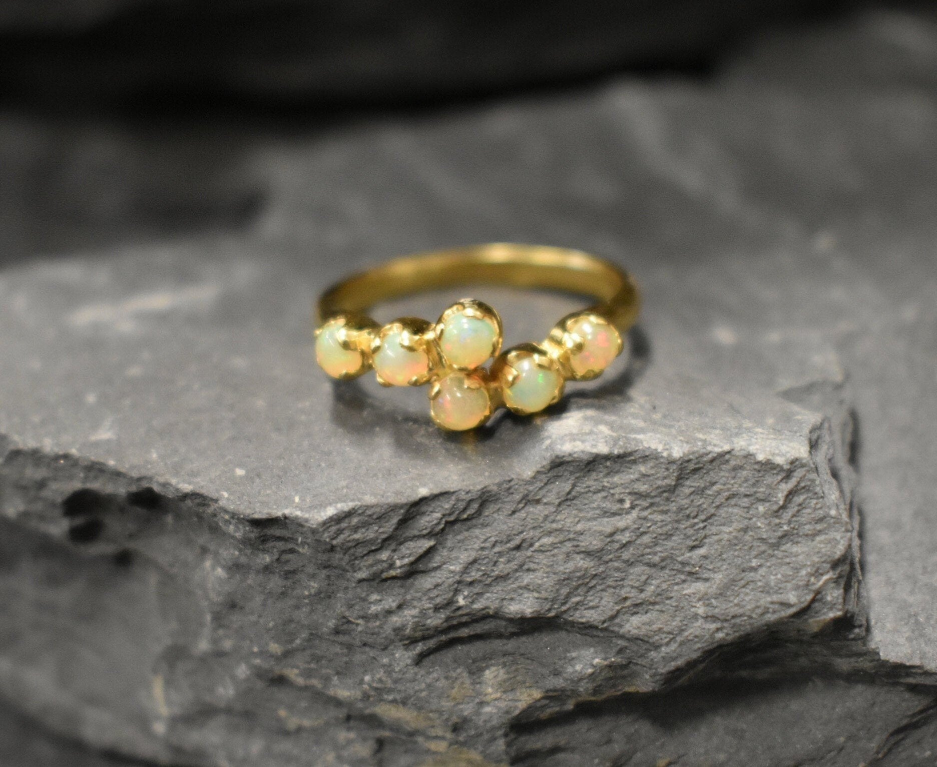 Ethiopian Opal Bypass Ring in gold with six cabochon stones aligned in a curved wrap setting, a stylish jewelry design that radiates flashes of fire colors and adds a modern edge, making it a thoughtful October birthstone gift idea. Perfect to wear at weddings, cocktail parties, and romantic dinners for a bold yet refined look.